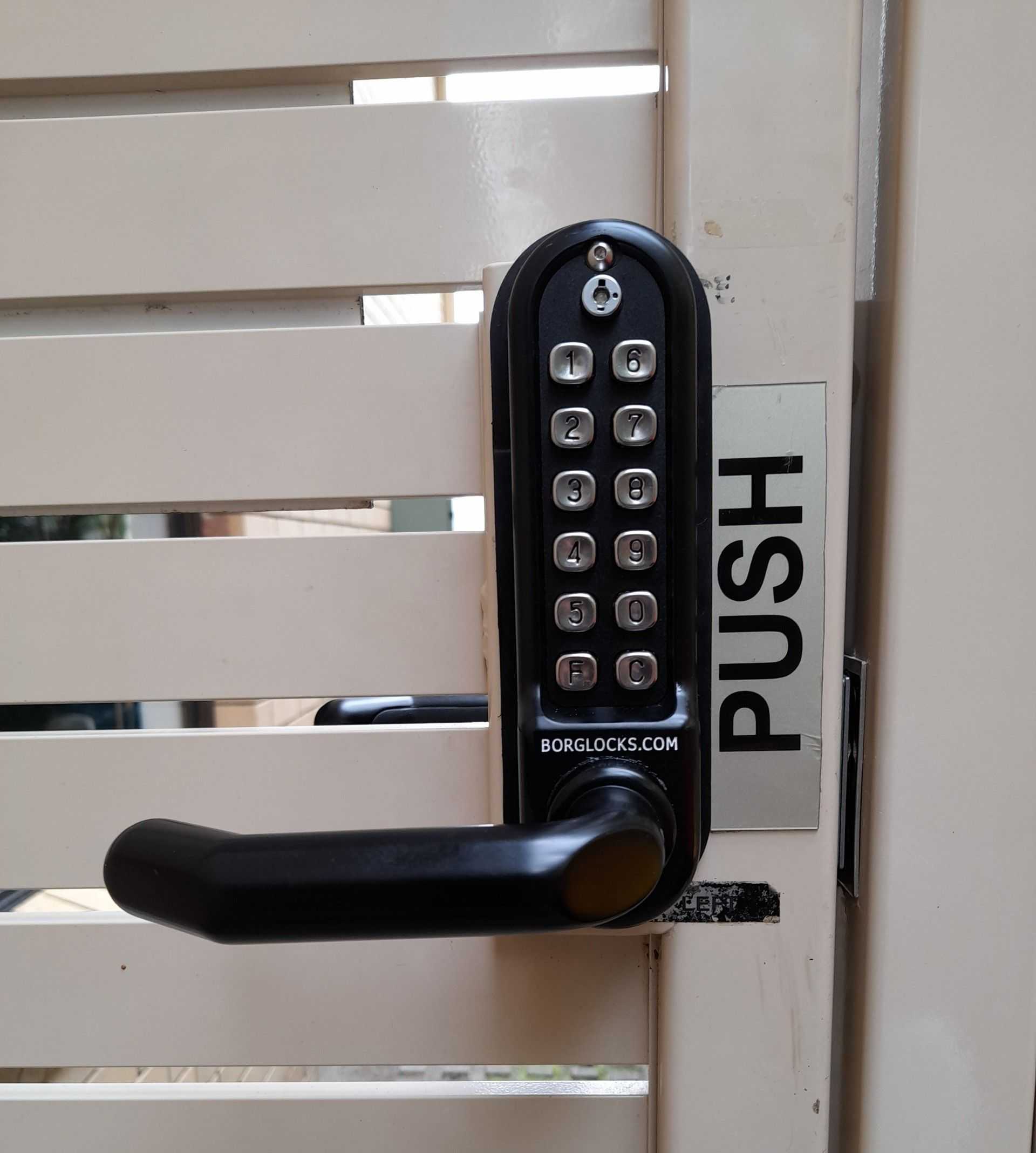 Black keypad lock with handle on a beige gate, 