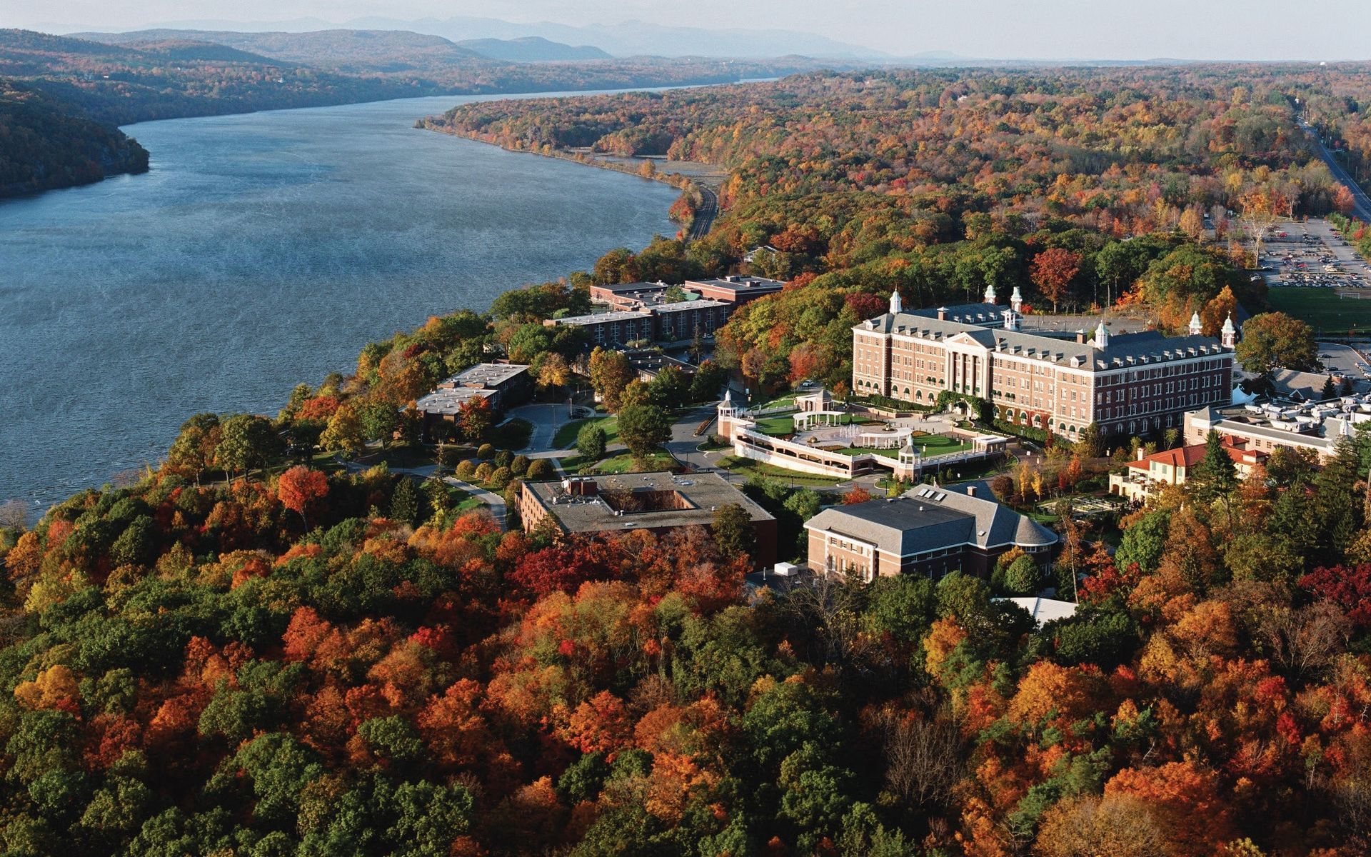 Aerial view of a riverside campus beside an autumn forest and wide river