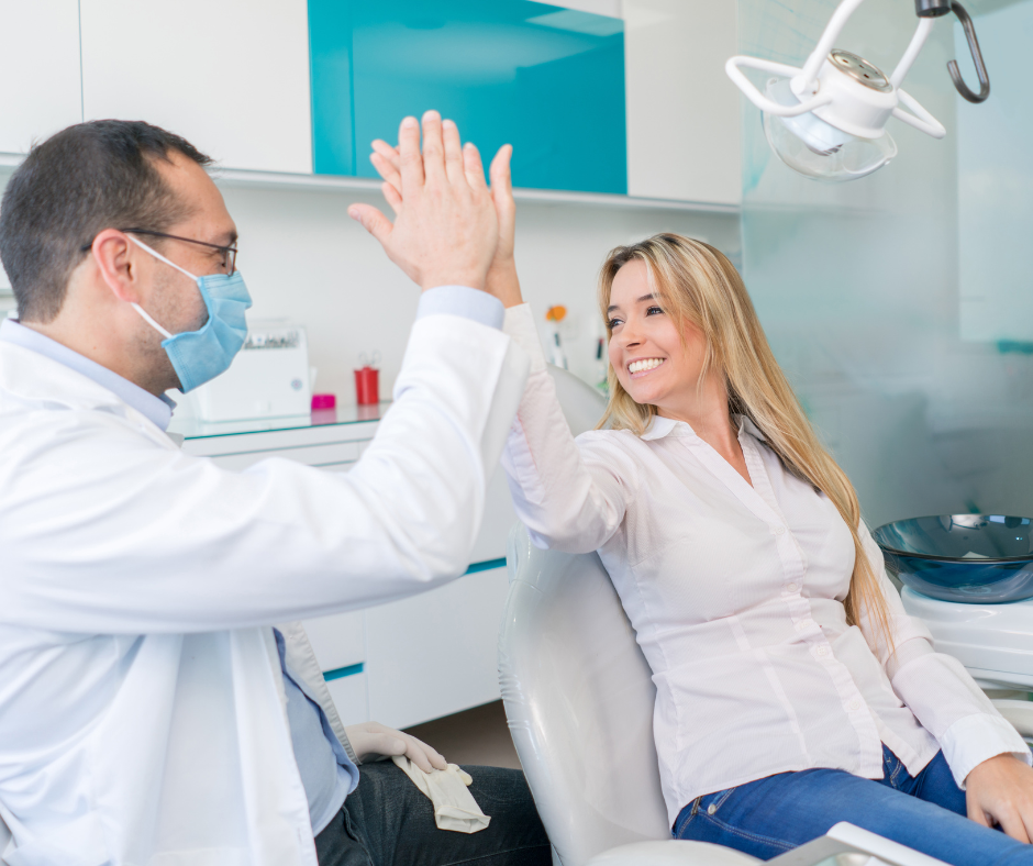 Dentist and patient high-five in a bright dental office, both wearing masks and smiling.