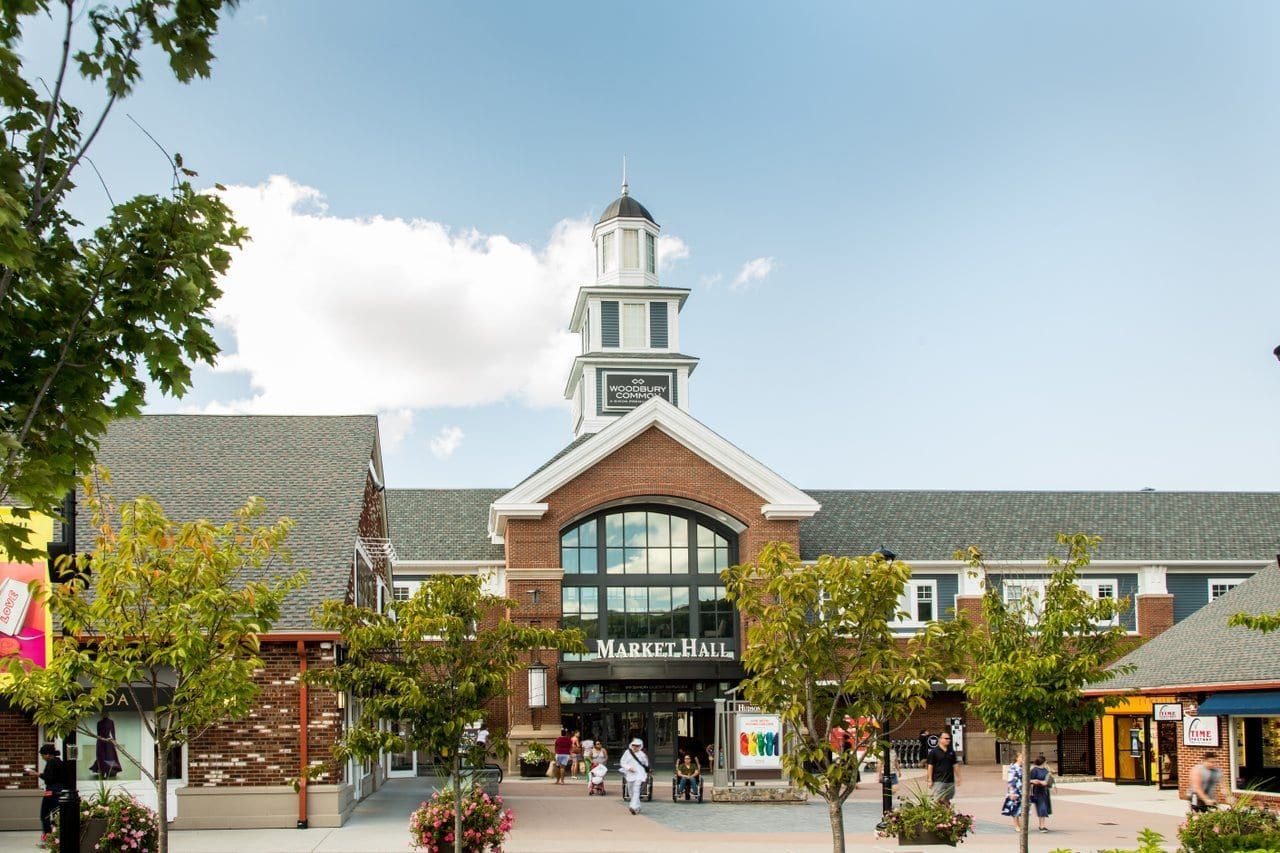 Shopping center entrance with clock tower, brick facade, and people walking in a plaza