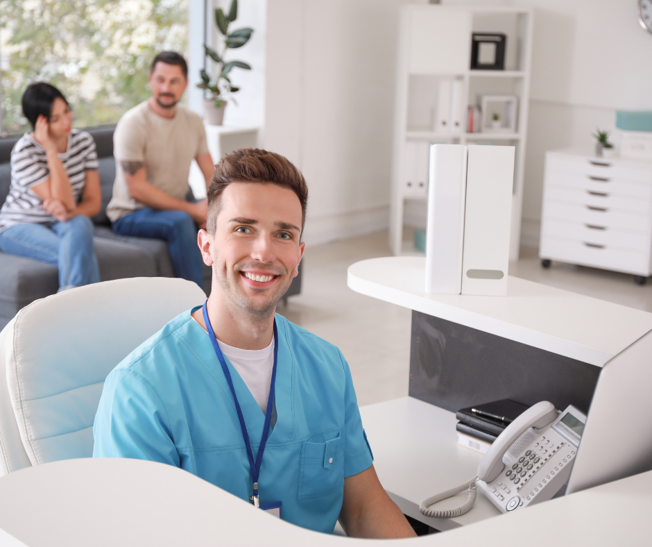 Dentist smiling at reception desk with patients waiting in the background