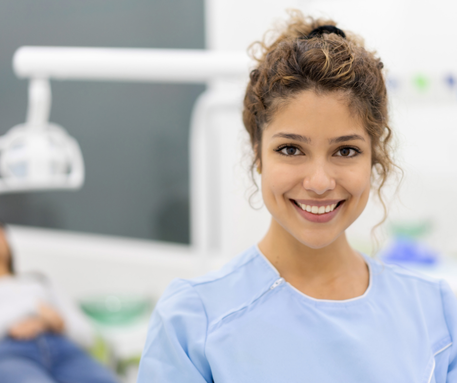 Two medical staff in a clinic, one in blue scrubs smiling and talking with a colleague.