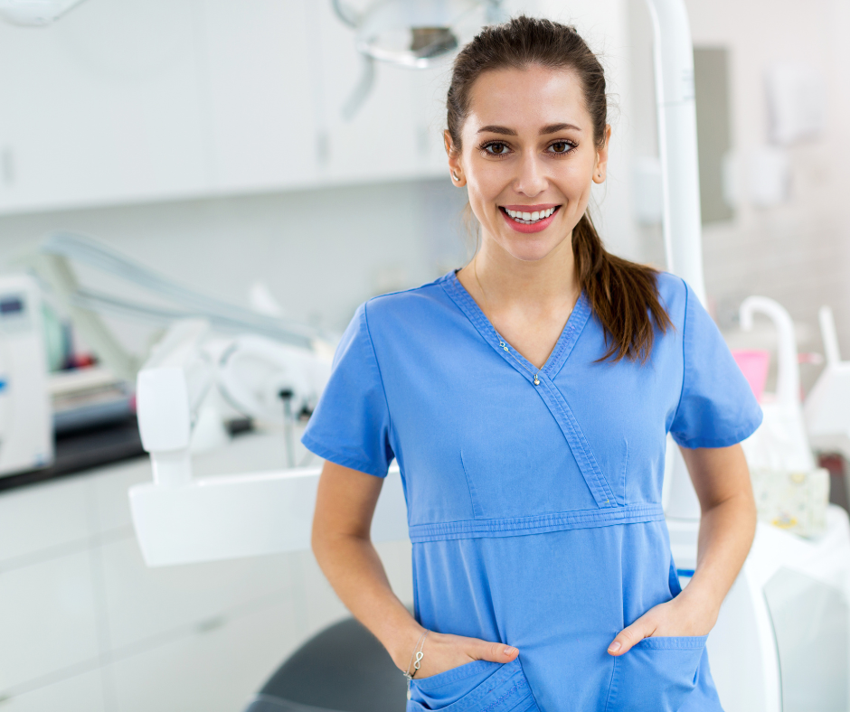 Two medical staff in a clinic, one in blue scrubs smiling and talking with a colleague.