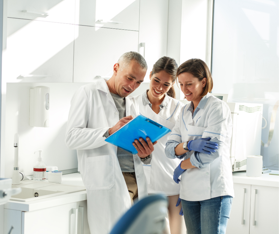Three lab workers in white coats review notes together in a bright laboratory.