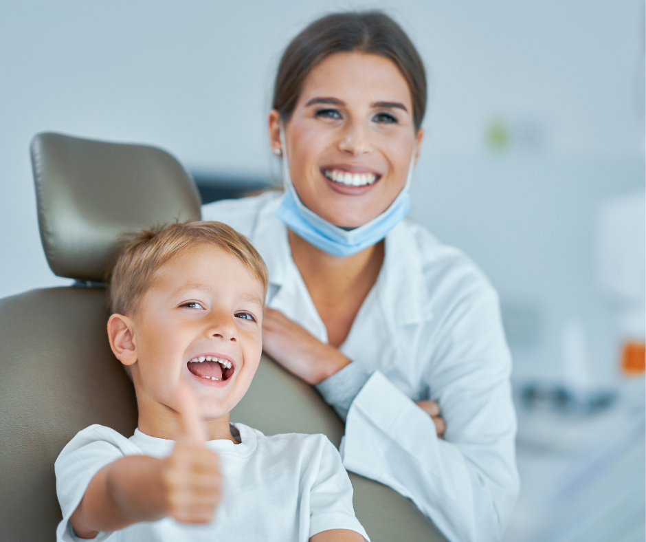 Smiling dentist with child in dental chair, child giving a thumbs-up