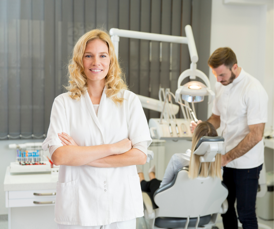 Smiling dentist in white coat with assistant working on a patient in a dental clinic