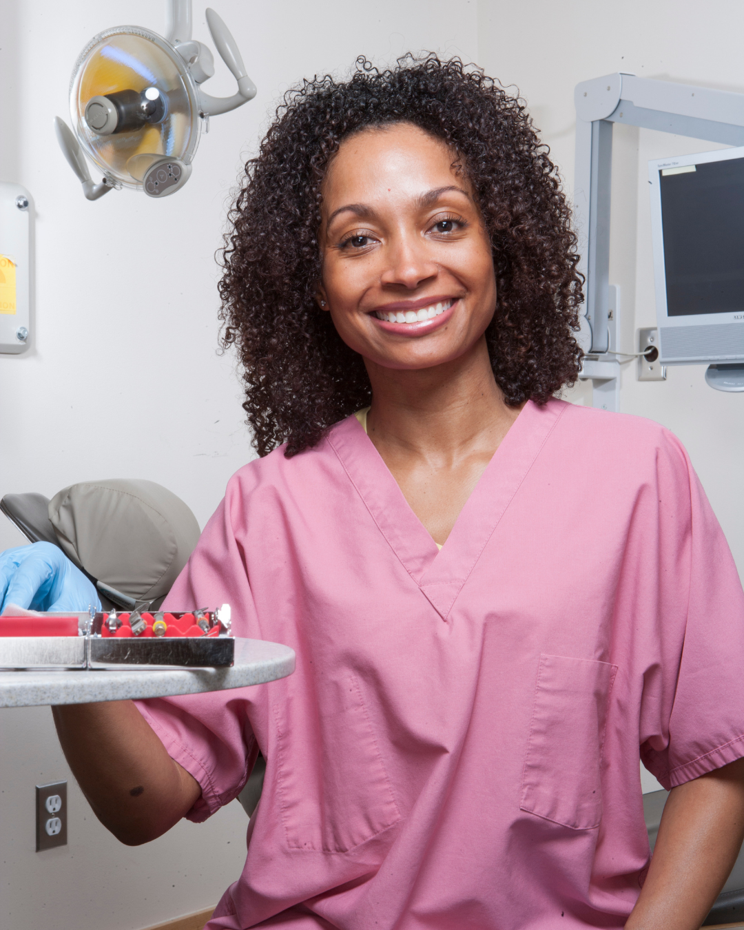 Two medical staff in a clinic, one in blue scrubs smiling and talking with a colleague.