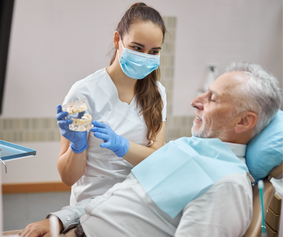 Dentist in blue gloves showing a dental mold to a reclining patient in a clinic