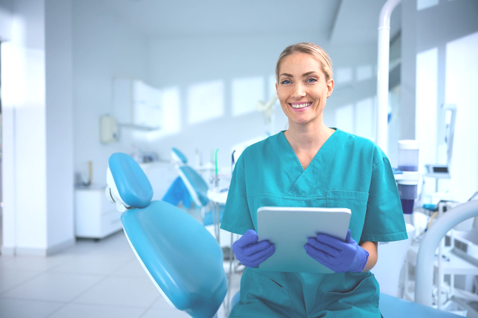 Two medical staff in a clinic, one in blue scrubs smiling and talking with a colleague.
