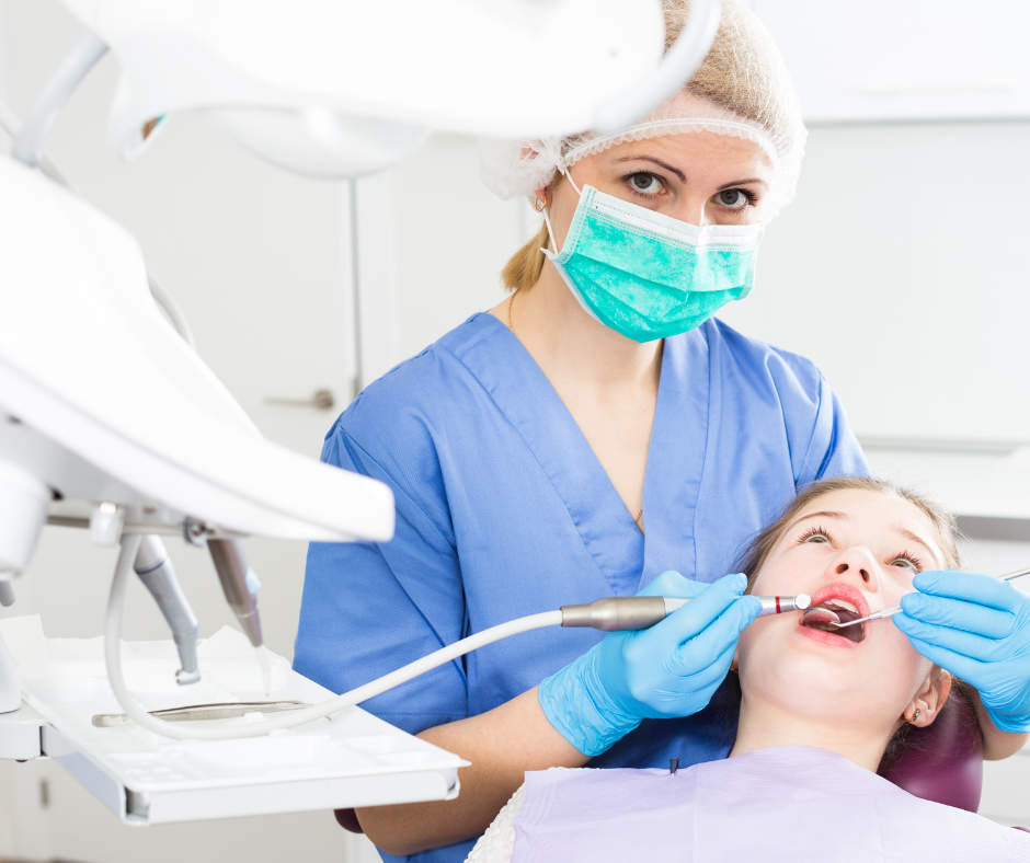 Dentist in blue scrubs and mask examining patient during dental treatment in a bright clinic
