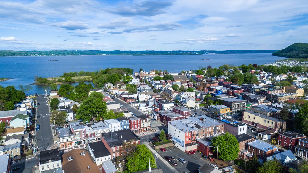 Aerial view of a coastal town with colorful buildings, streets, and a large blue bay under a clear sky