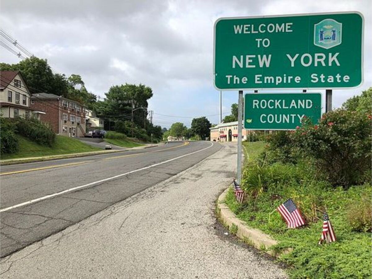 Welcome to New York State sign at Rockland County roadside entrance, with small American flags.