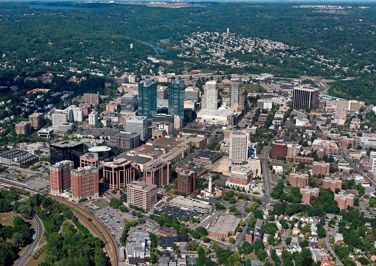 Aerial view of a downtown skyline with mid-rise buildings, streets, and surrounding green neighborhoods