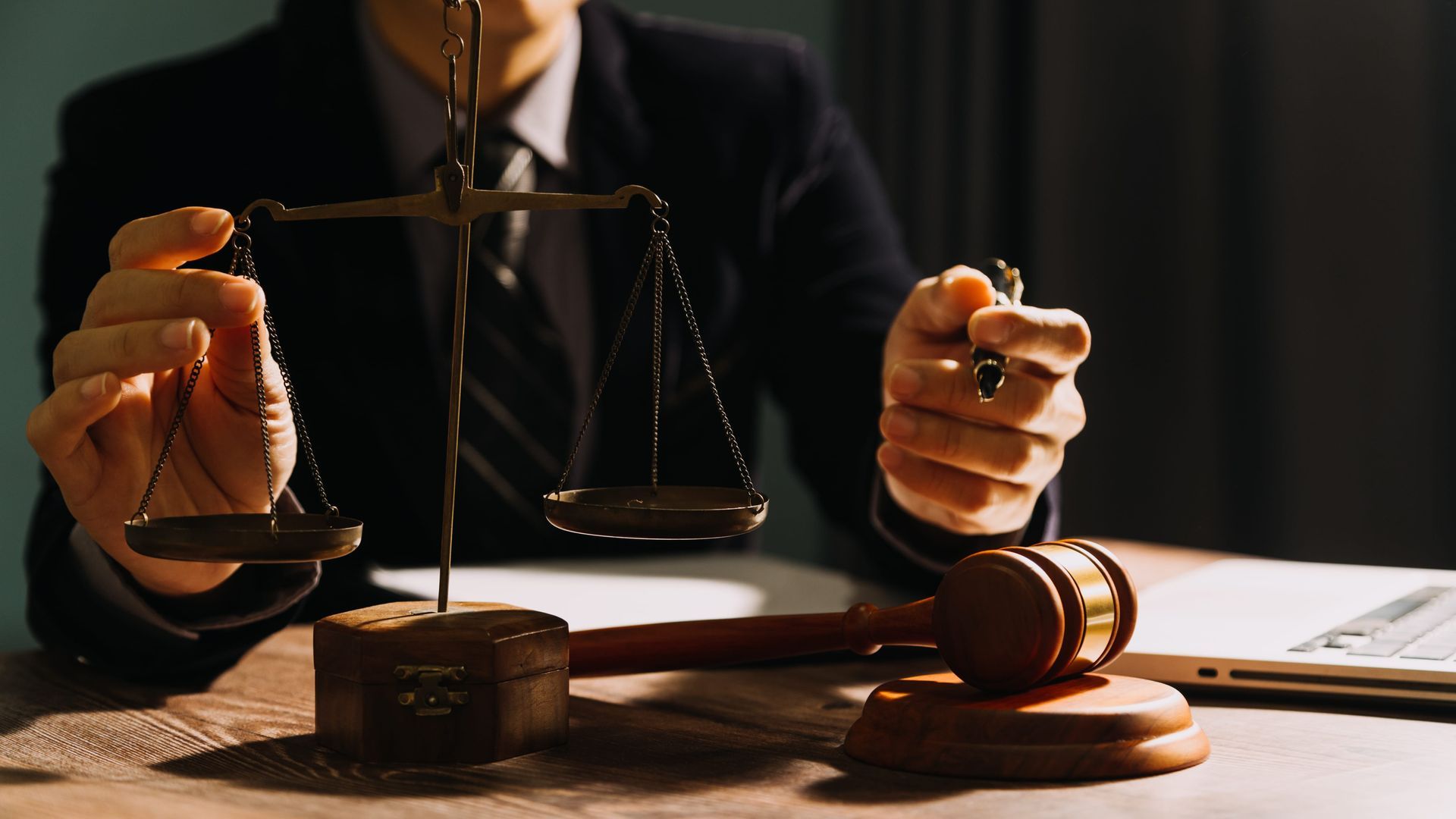 Lawyer’s hands holding scales and gavel over a desk with legal papers in warm light