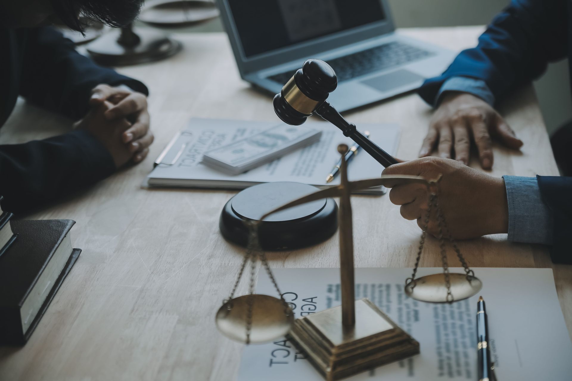 Legal meeting with gavel and scales on a desk, two people discussing beside a laptop and documents