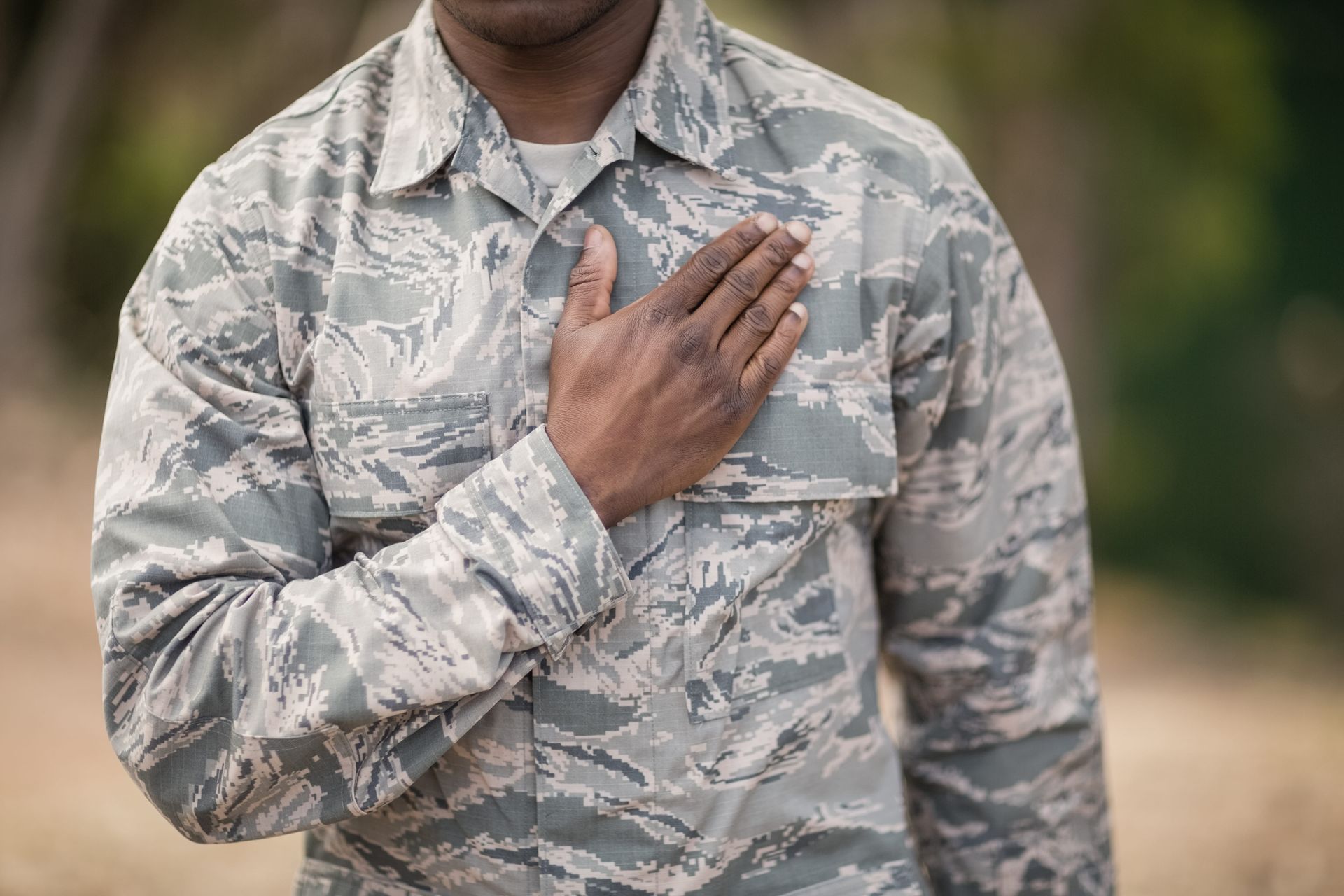 Person in camouflage uniform with hand over chest outdoors