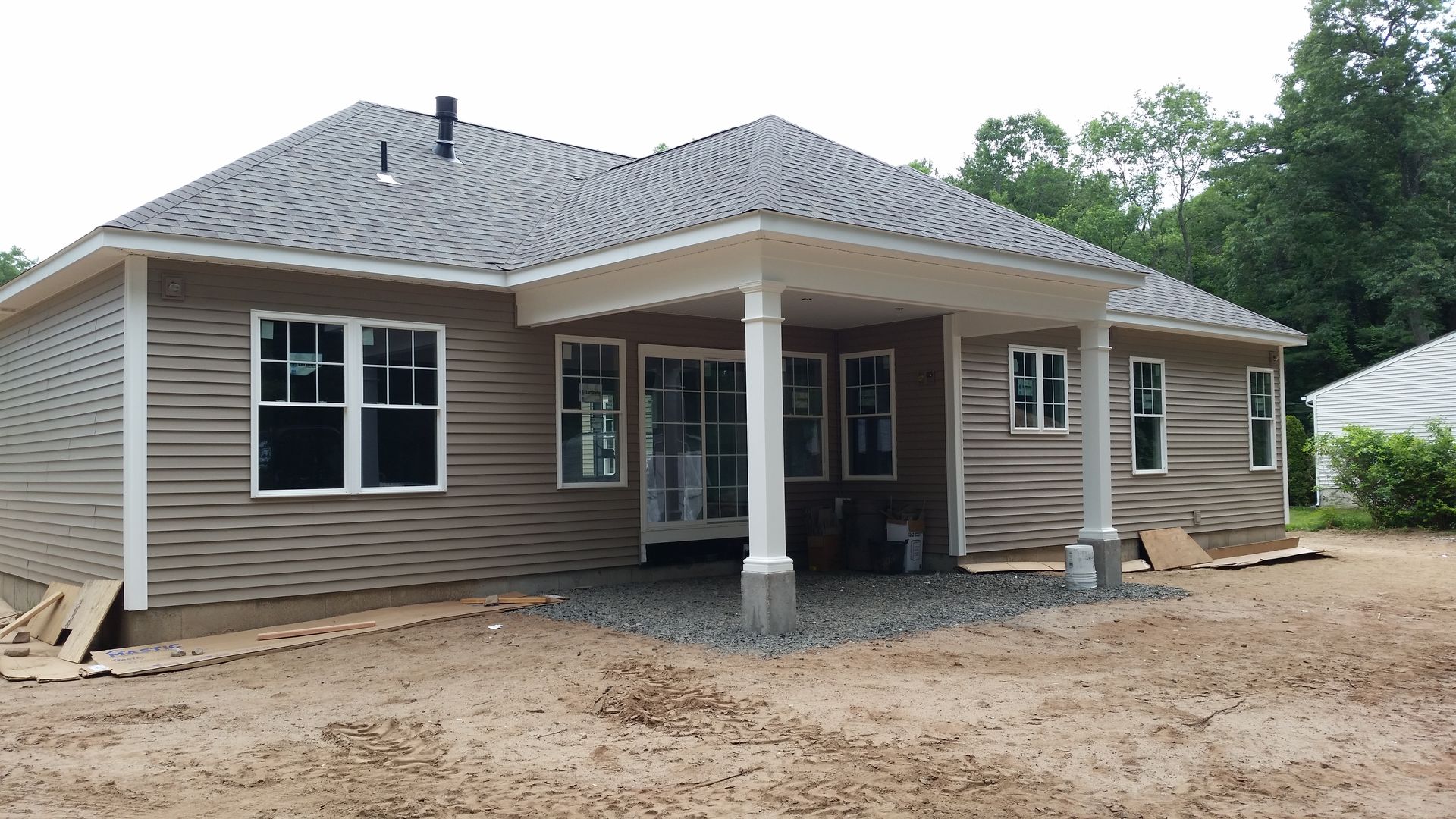 Tan house with gray roof, a covered patio, windows, and unfinished ground.