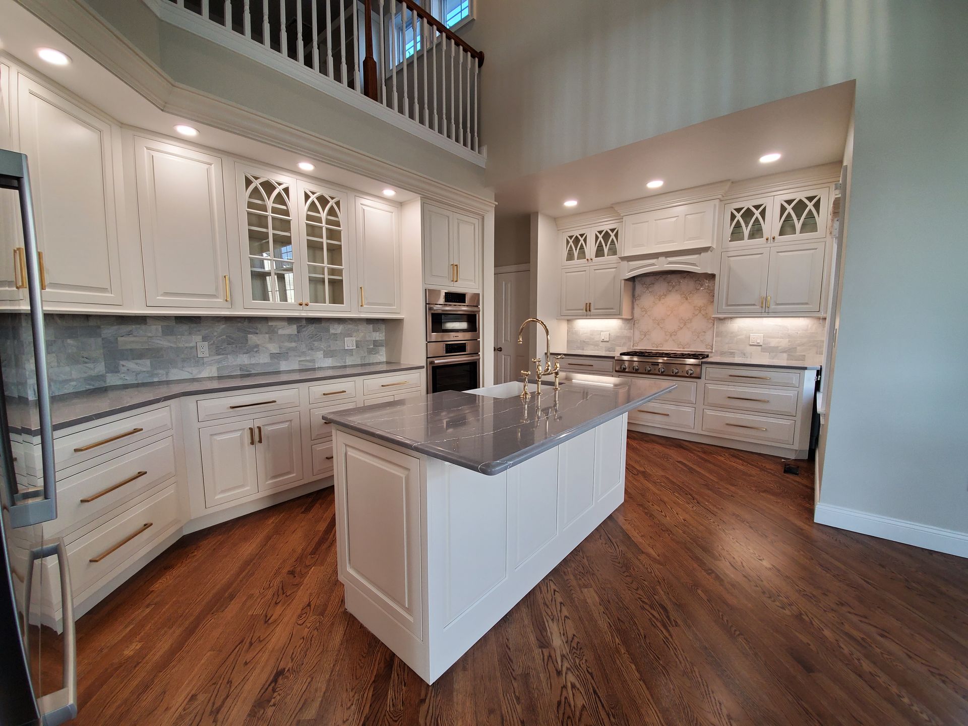 Elegant white kitchen with a large island, wood floors, and a second-floor overlook.