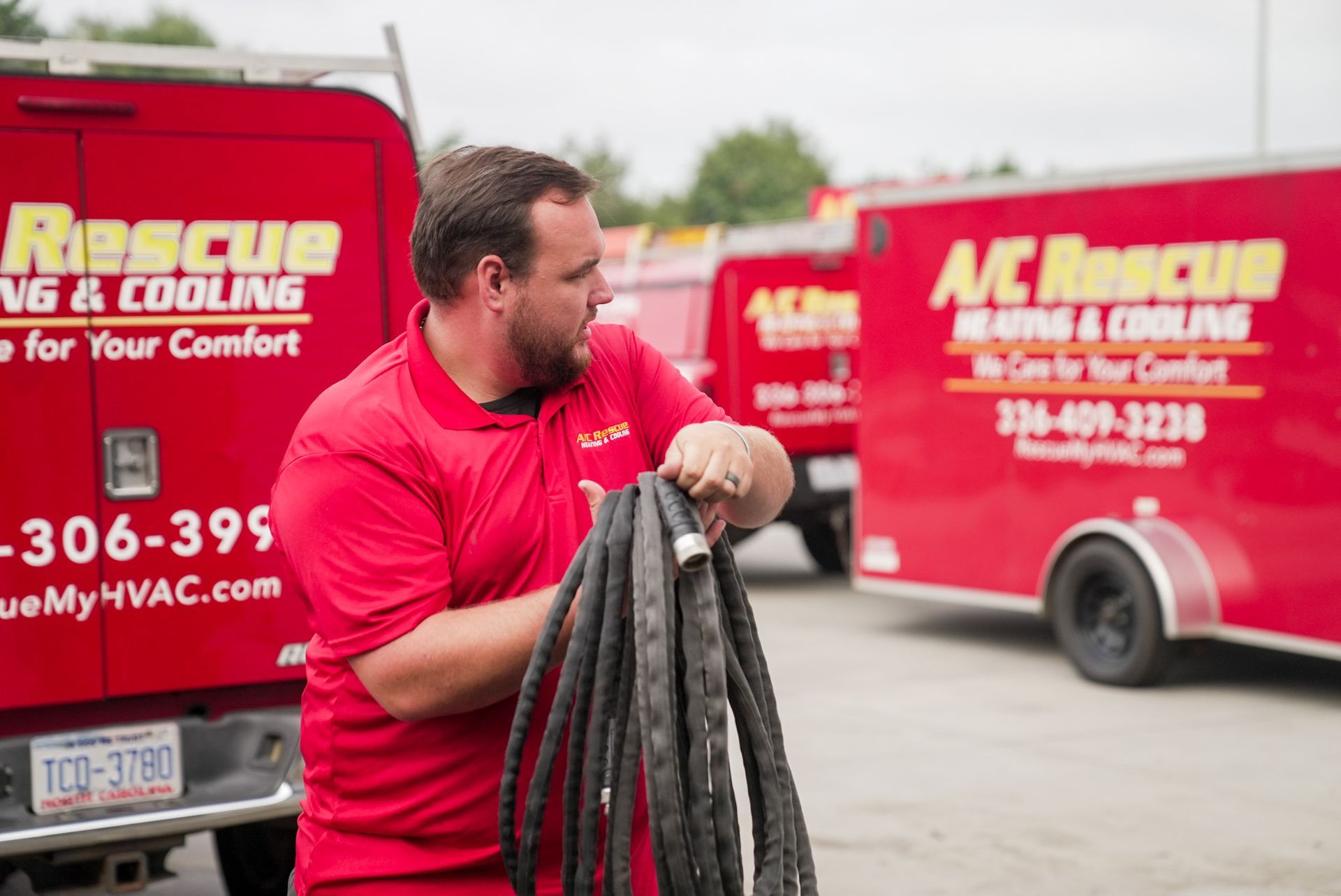 Worker in red shirt holding coiled cable beside McRescue HVAC service van outdoors