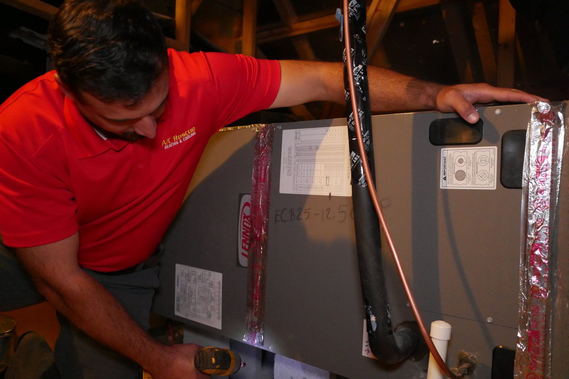 Technician in red shirt inspecting HVAC equipment in a utility room.