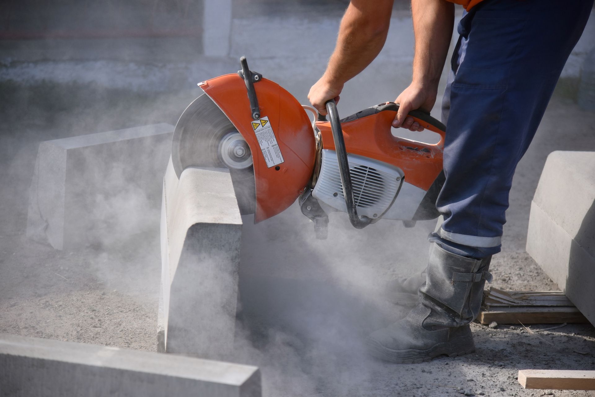 A worker cuts a curb with a circular saw, to repair the road.