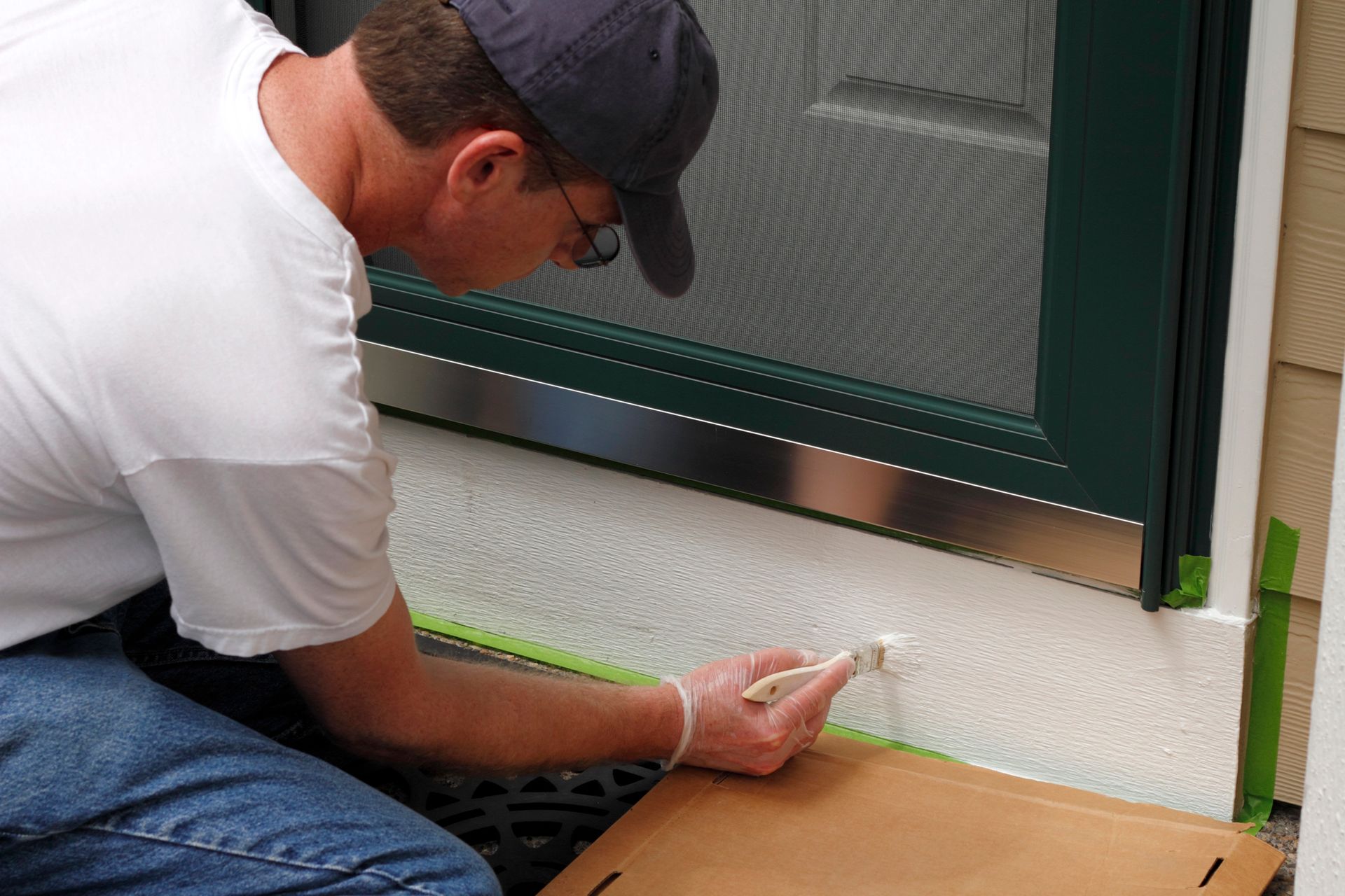 Person painting along the bottom of a green door frame outdoors.