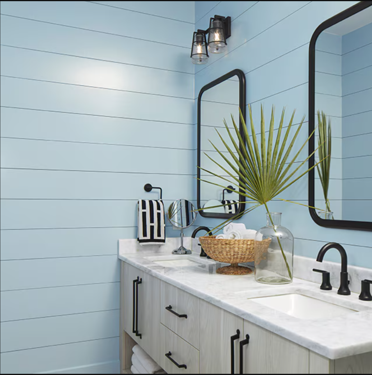 Light blue bathroom vanity with black fixtures, white countertop, mirror, and decorative palm leaf.