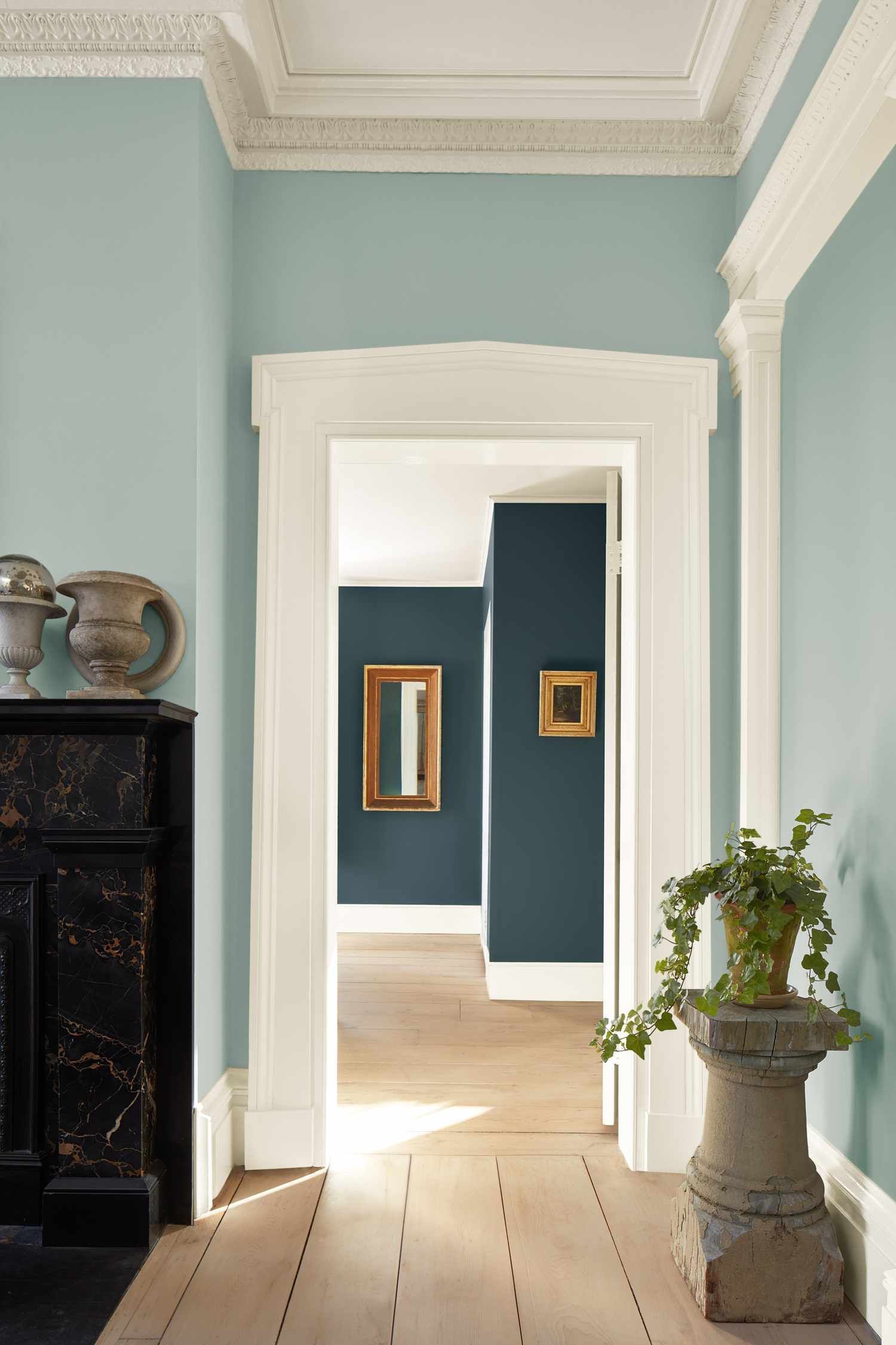Elegant hallway with pale blue walls, white trim, framed artwork, and a potted plant on a pedestal