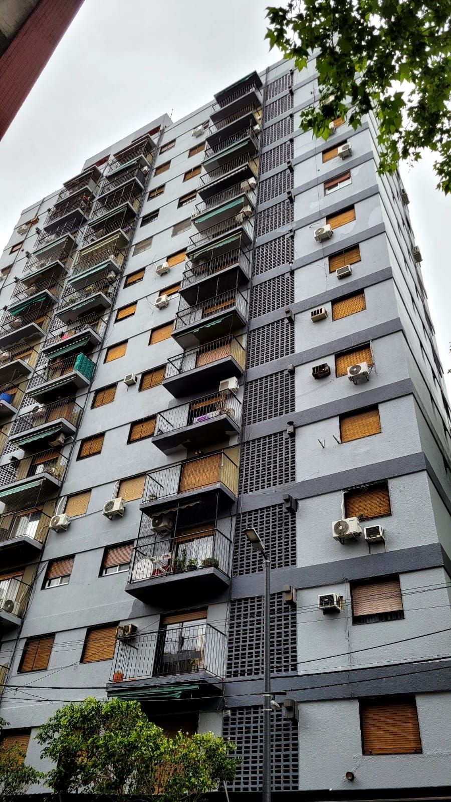 Edificio de apartamentos alto y gris en una calle arbolada de la ciudad con coches aparcados en la planta baja.