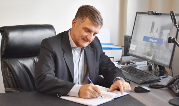 Hombre con traje escribiendo en un escritorio con una computadora y un teléfono en una oficina.