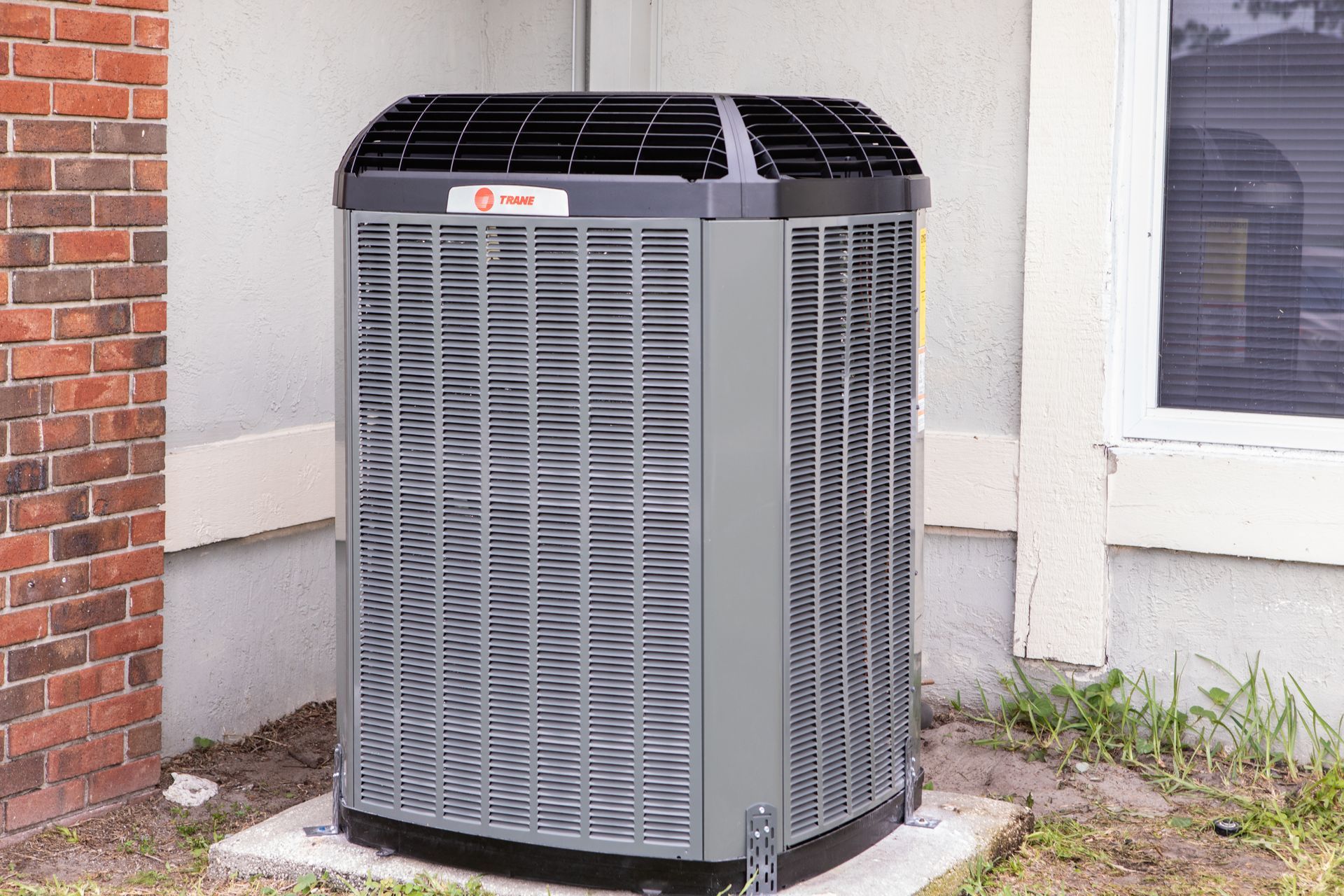 Outdoor air conditioning unit beside lush green plants and a small utility box.