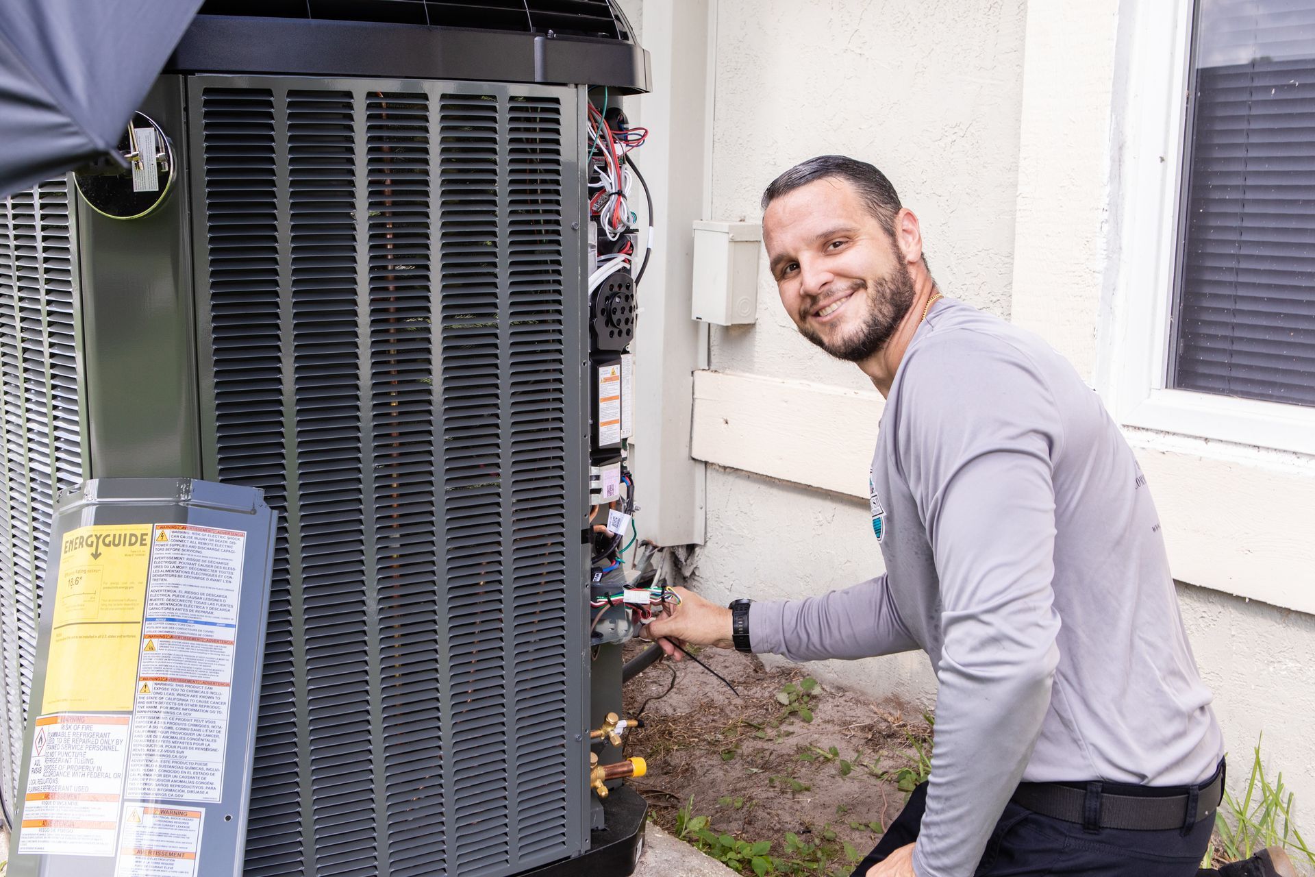 Technician in blue cap repairing an outdoor air conditioner unit with tools