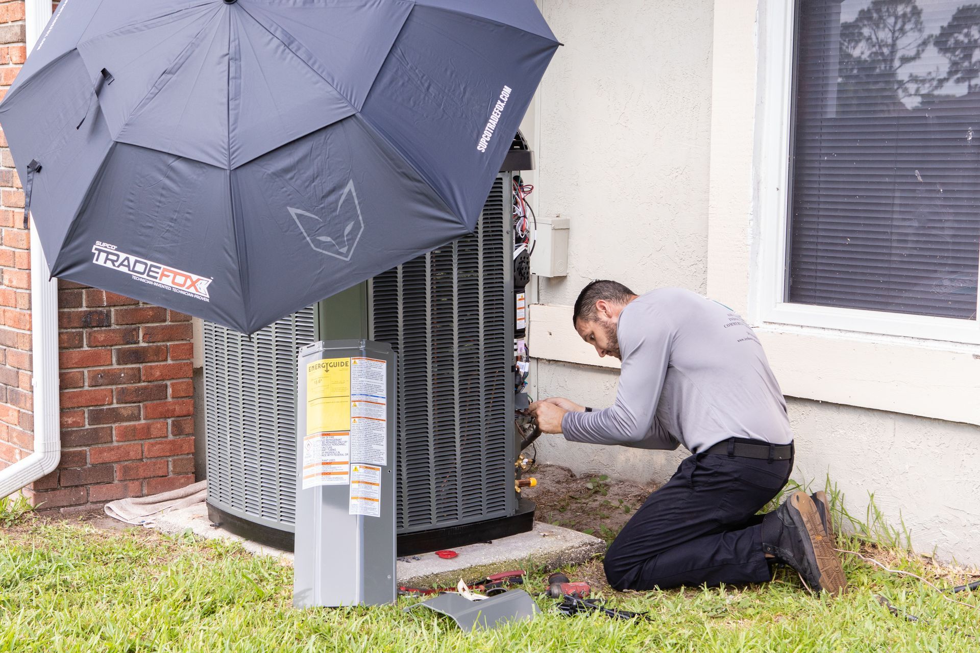 Technician in blue uniform inspecting a window air conditioner with the front panel open