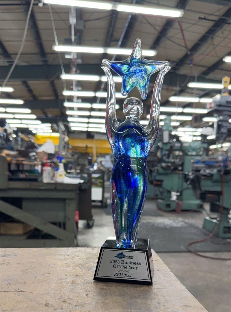 Glass award, a figure holding a blue star, on a black base.  In an industrial setting.