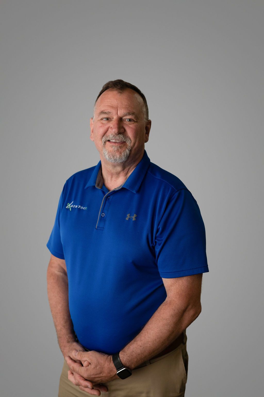 J.D. Wildt in blue polo shirt, arms crossed, smiling, standing against a gray backdrop.