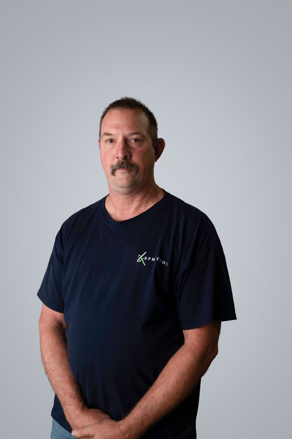 Kenny Ball wearing a dark blue t-shirt with a logo, standing in front of a neutral background.