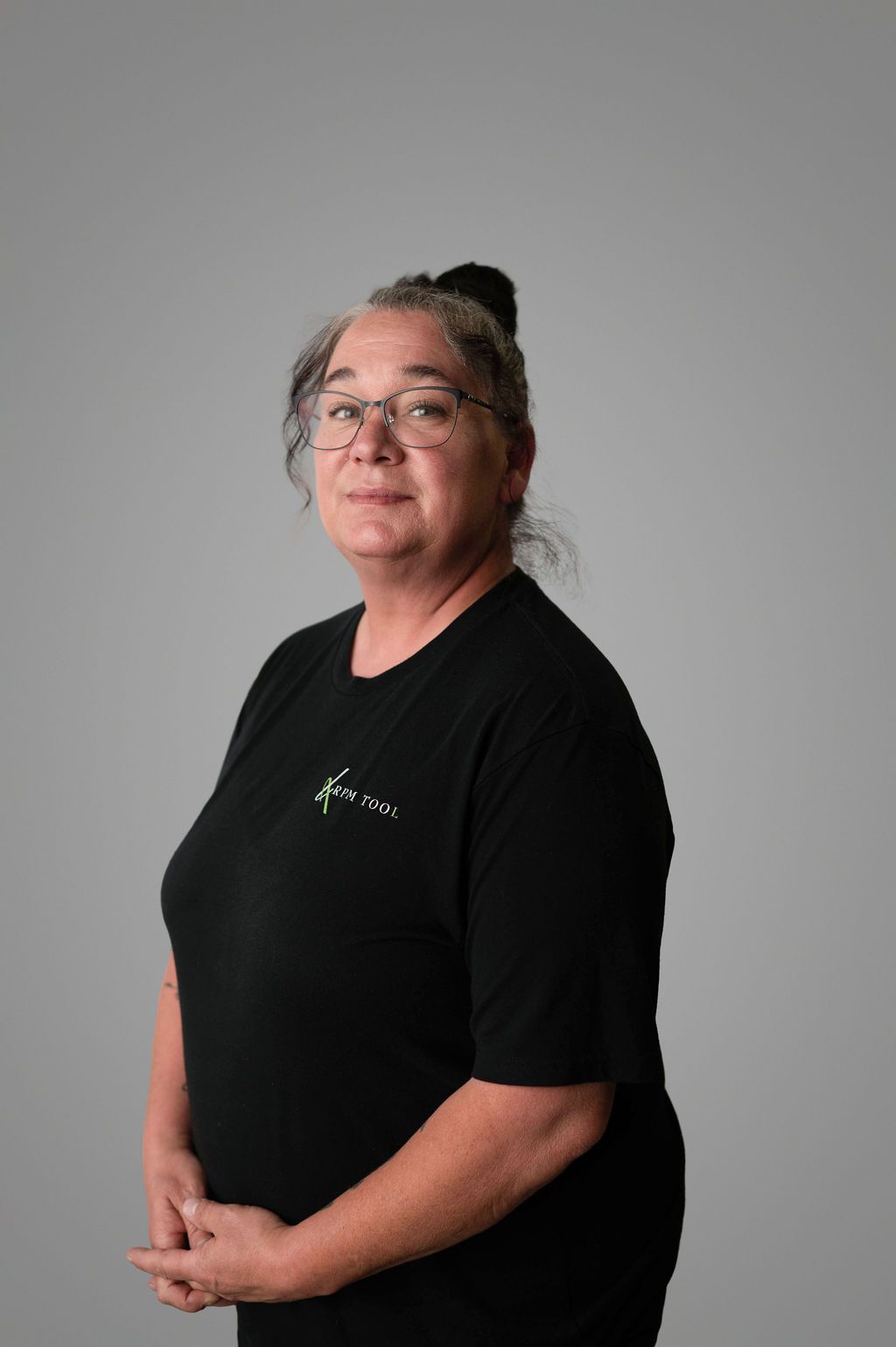 Shannel Whitehead with glasses, black t-shirt, arms crossed, standing in front of a gray backdrop.