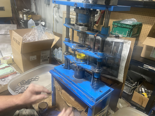 Blue industrial press with hands, inside a cluttered workshop.