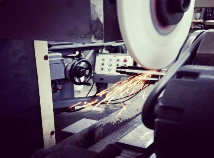 Grinding machine in use, sparks flying. A metal object is being sharpened by a rotating abrasive wheel.