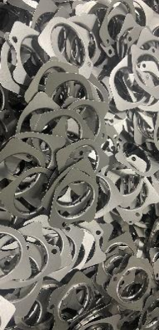 Pile of metal gaskets with irregular shapes and circular cutouts.