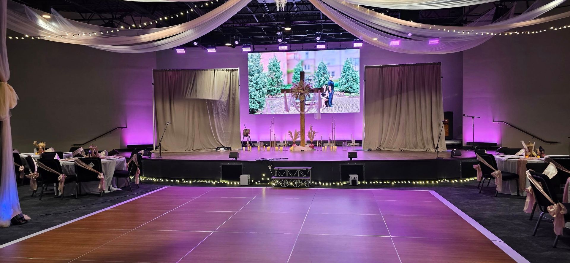 A stage set for an event with a large screen displaying a cross, curtains, and seating areas.
With Love, Wedding management, Milwaukee Wedding Coordinator