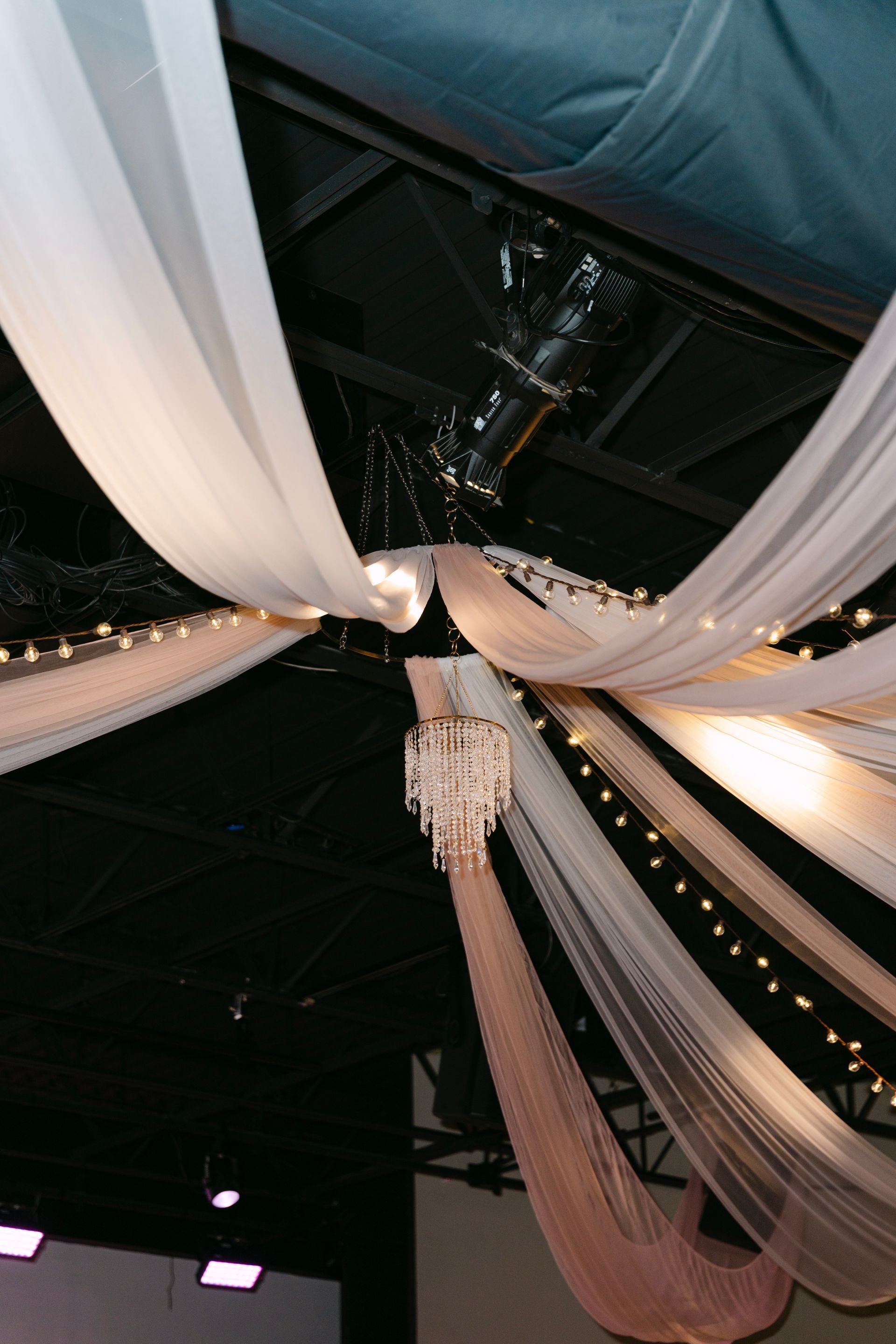 Sheer fabric drapes from a black ceiling, a chandelier and string lights are suspended.
With Love, Wedding management, Milwaukee Wedding Coordinator