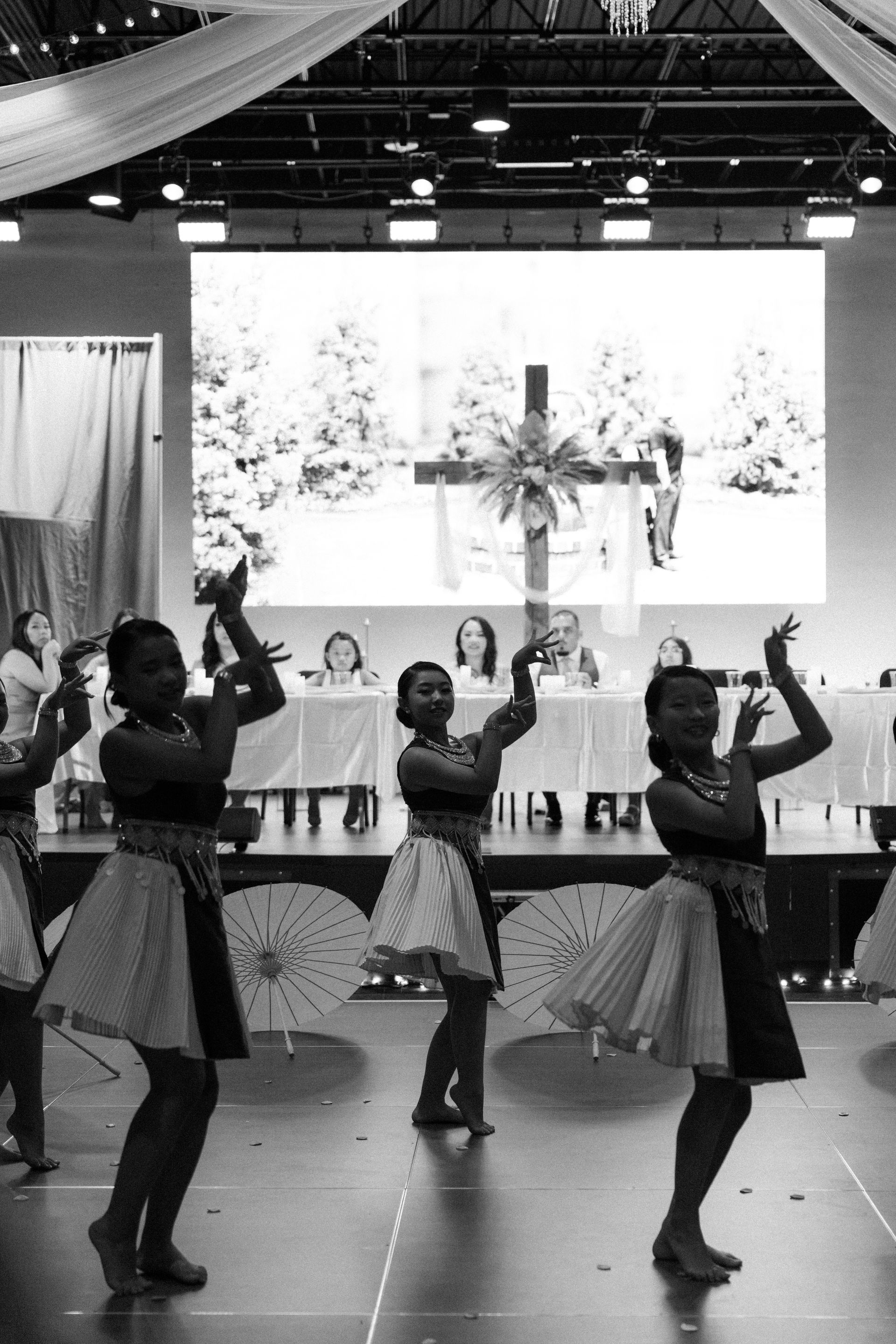 Dancers in skirts perform on stage; backdrop shows a cross. Interior setting.
With Love, Wedding management, Milwaukee Wedding Coordinator