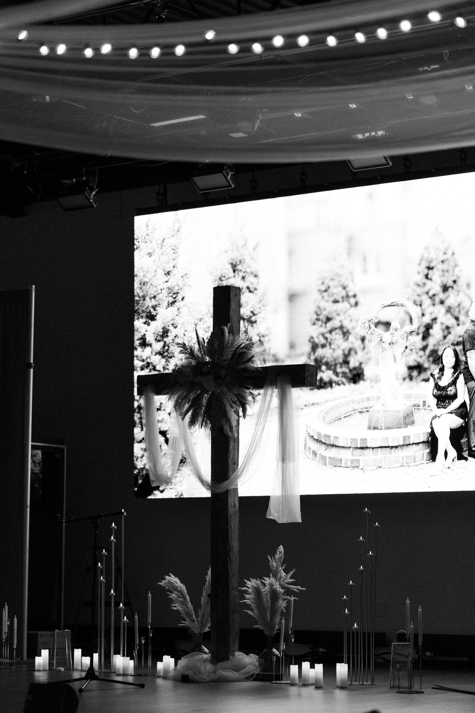 A wooden cross decorated with flowers and fabric, in front of a screen displaying a black and white image, candles.
With Love, Wedding management, Milwaukee Wedding Coordinator