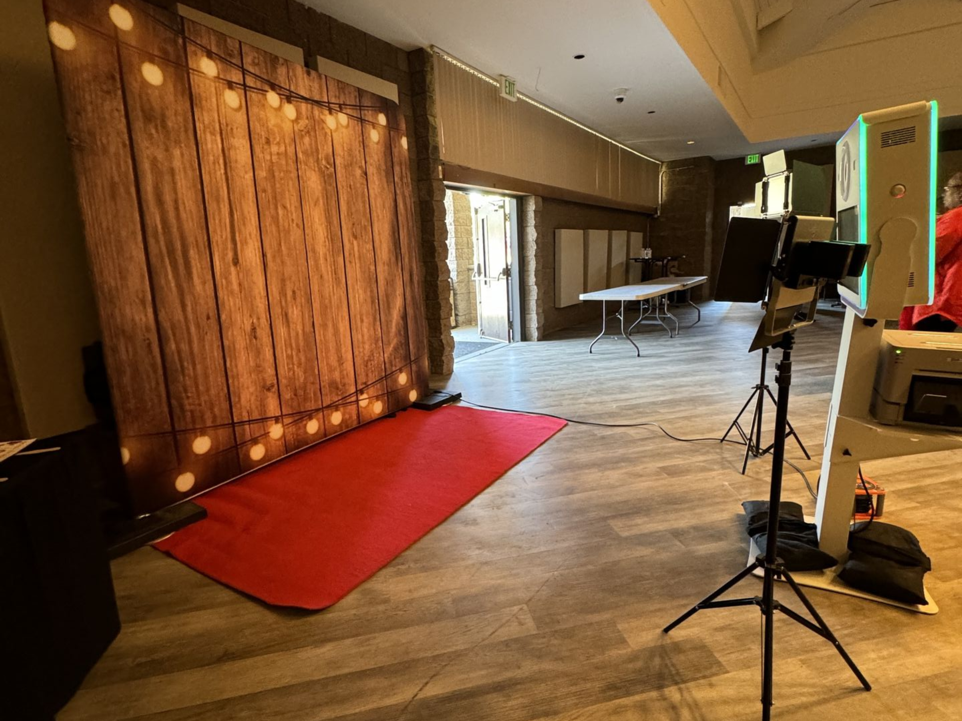 Empty event space with red carpet, wooden backdrop, and photography lighting setup.