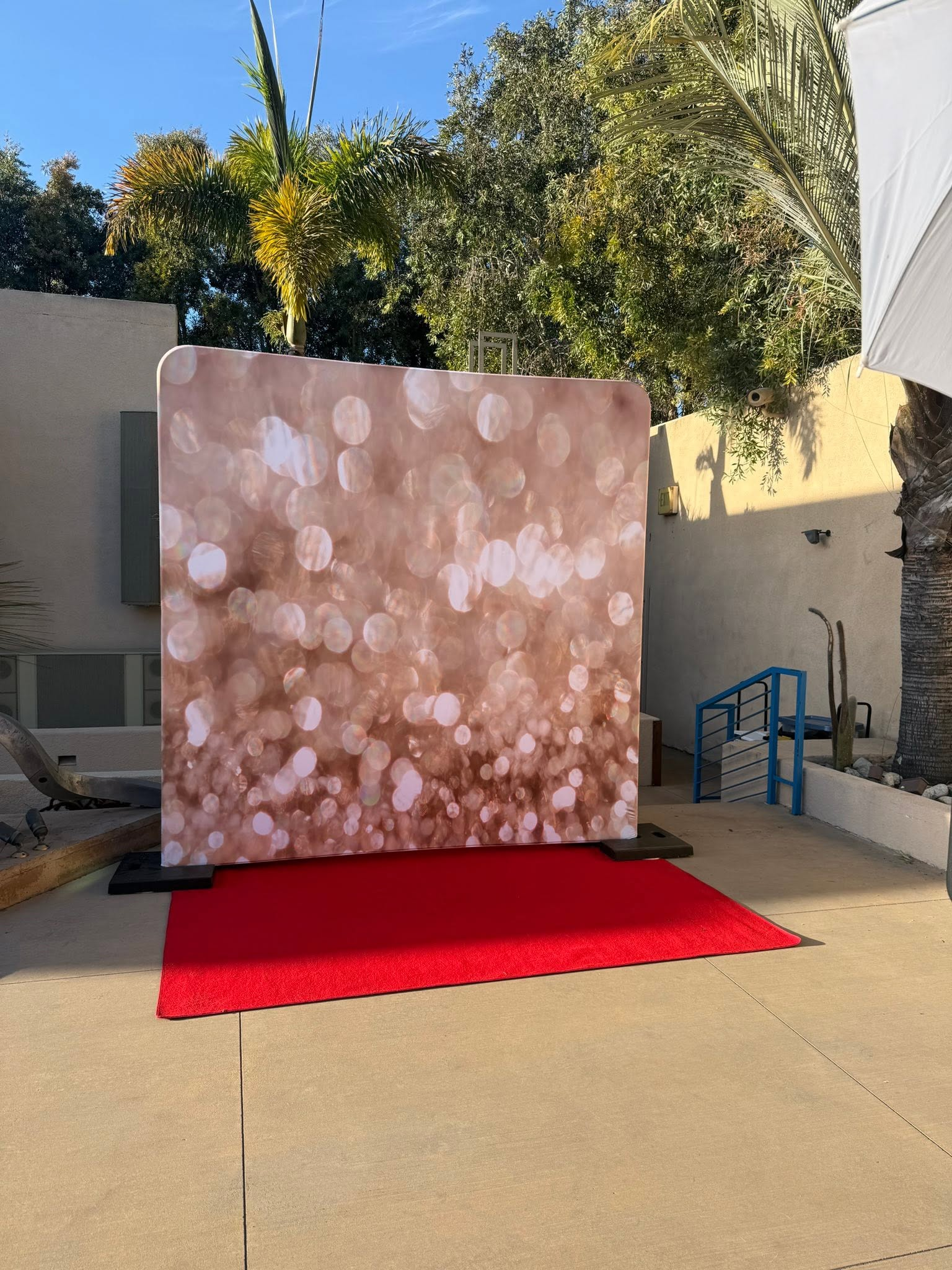 Outdoor photo backdrop with pink bokeh pattern on a red carpet in a courtyard.