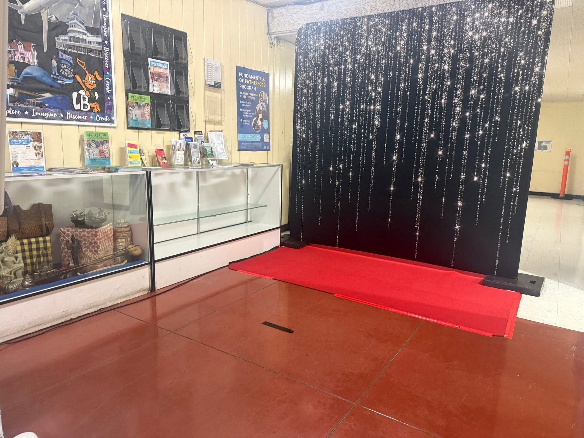 Small indoor display area with glass cases, posters, and a red-carpeted black curtain backdrop.