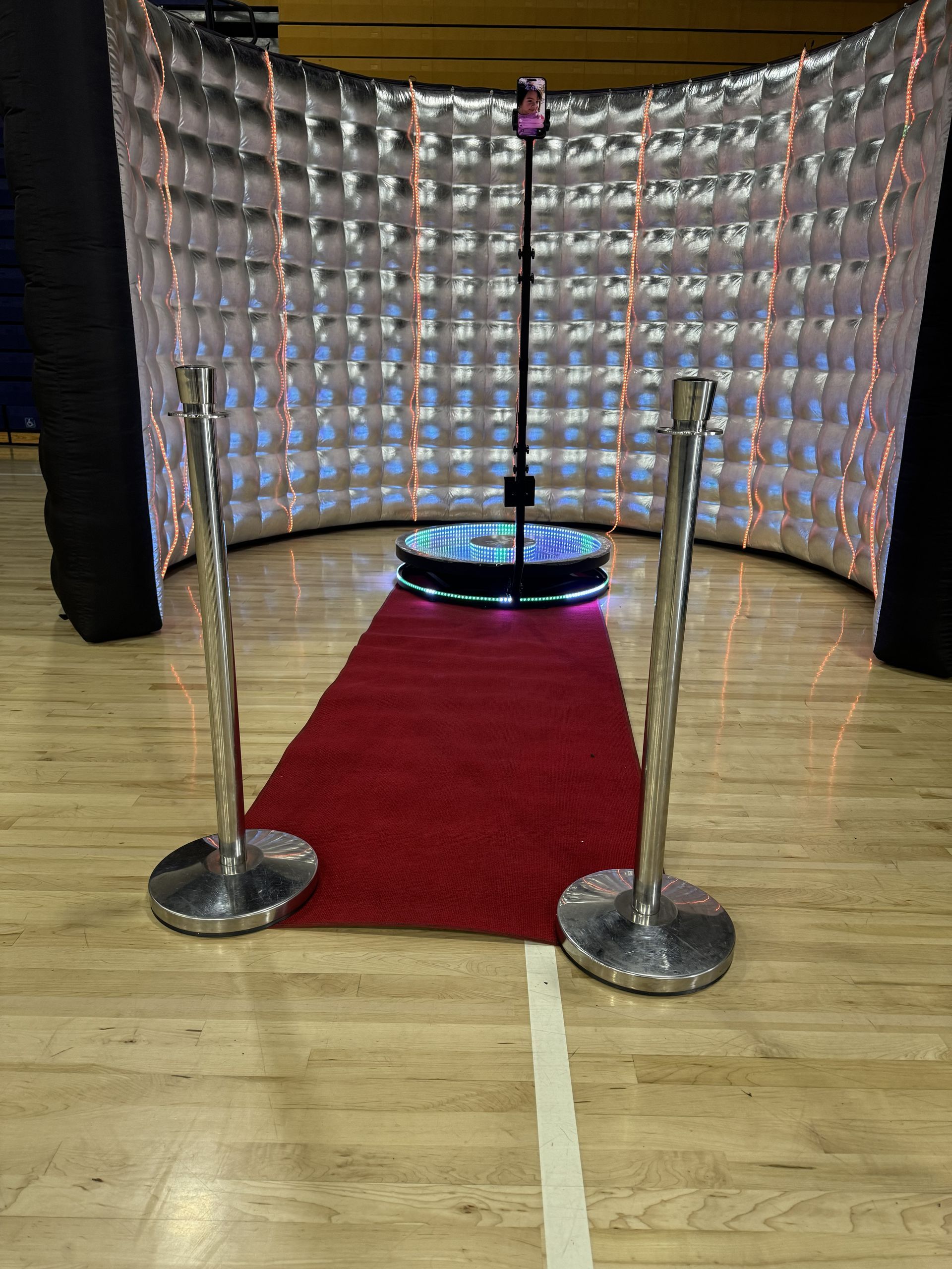 Red carpet leading to a small stage with a glowing circular light, framed by silver stanchions and a curved backdrop.