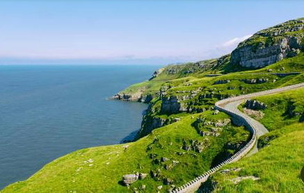 A road going through a lush green hillside next to the ocean.