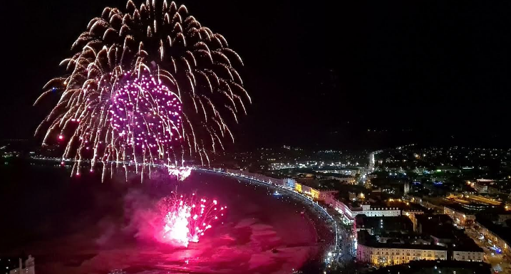 An aerial view of a fireworks display over a city at night.